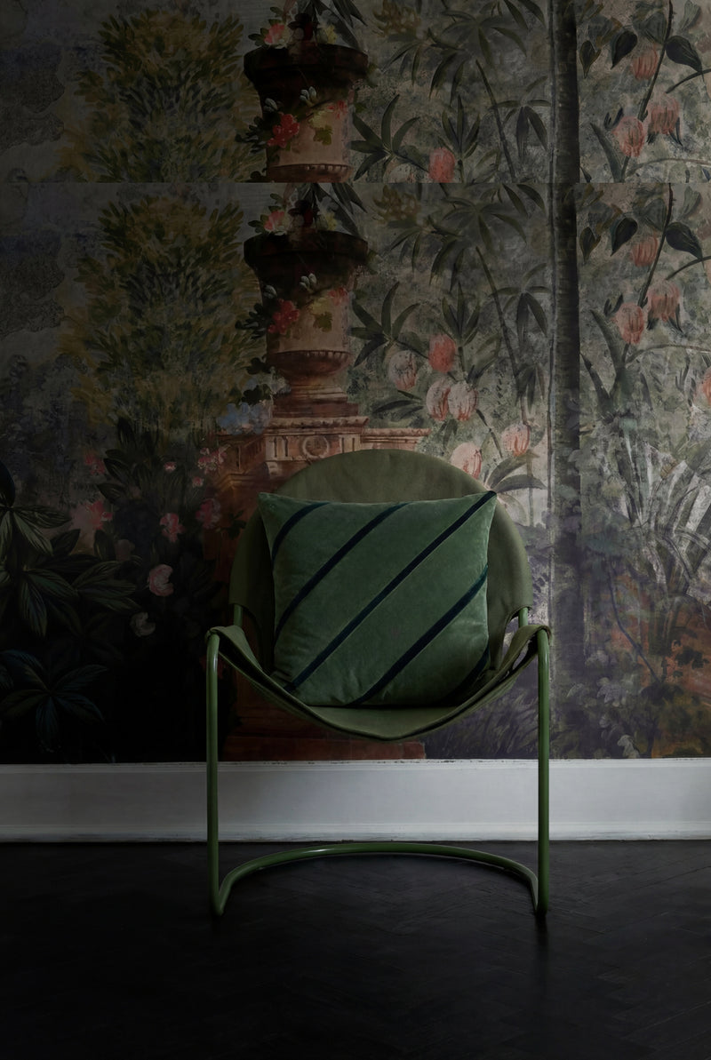 Green chair with a striped cushion against a floral wallpapered wall.
