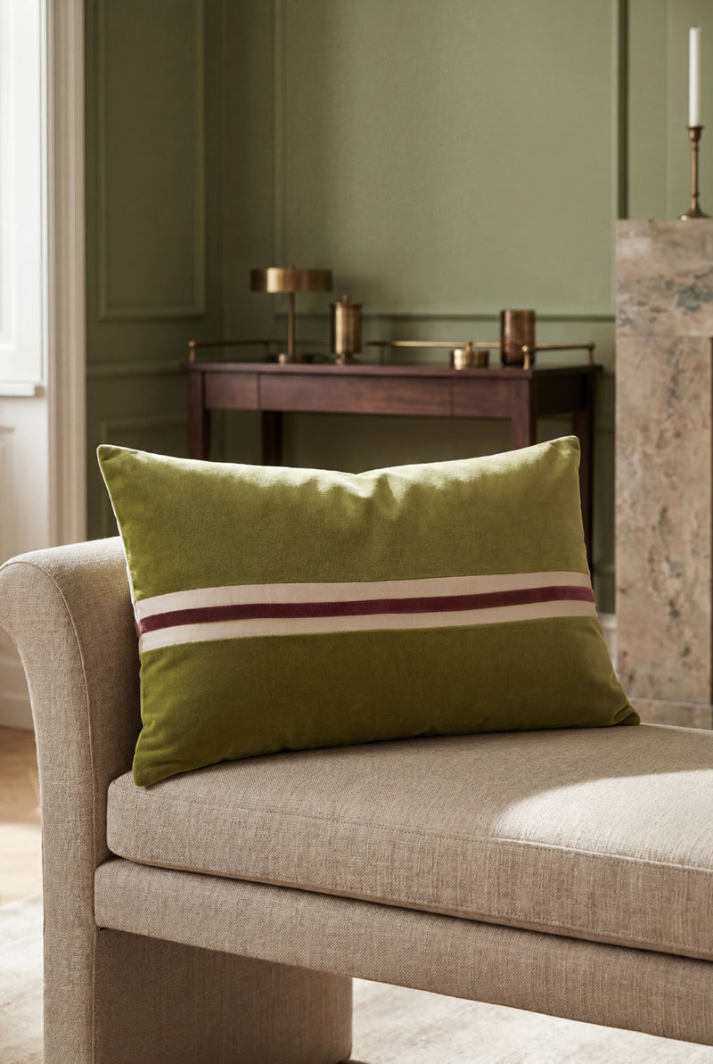 Green pillow with a red stripe on a beige sofa against a green wall.
